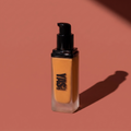 Liquid Foundation de YG Beauty, frasco con dosificador sobre fondo rosa arcilla