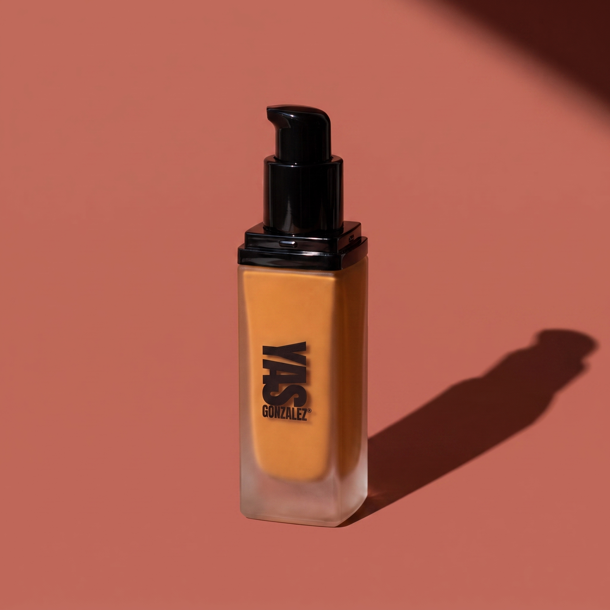 Liquid Foundation de YG Beauty, frasco con dosificador sobre fondo rosa arcilla