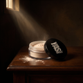 Finishing Powder de YG Beauty con su tapa y polvo derramado, luz de claroscuro