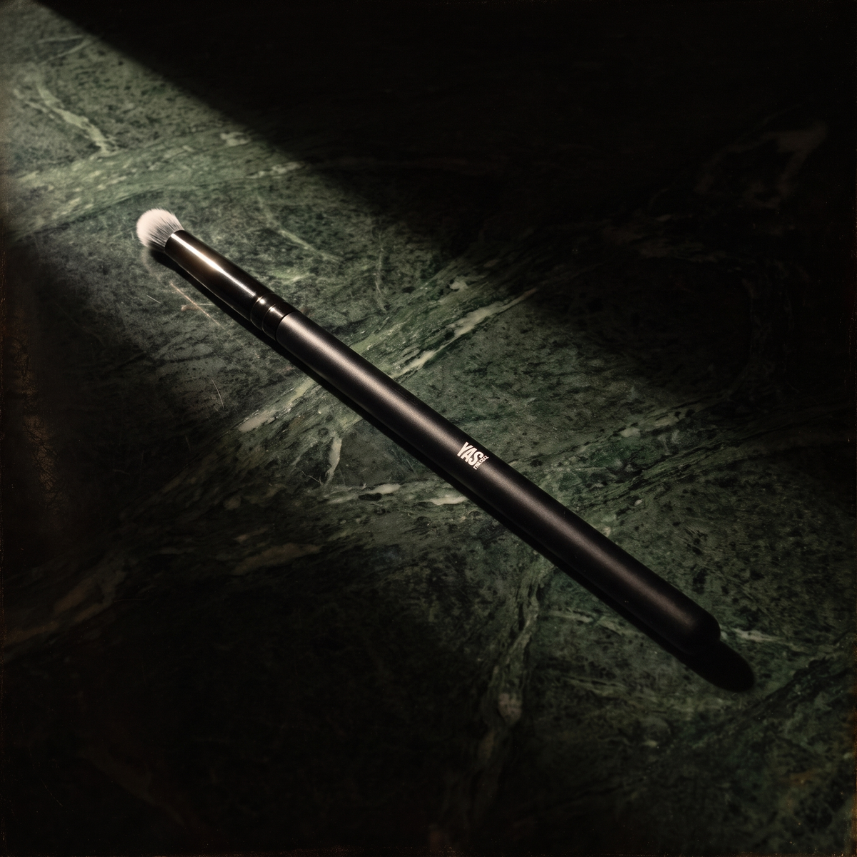 Mini Crease Brush de YG Beauty sobre mármol verde oscuro, luz de claroscuro