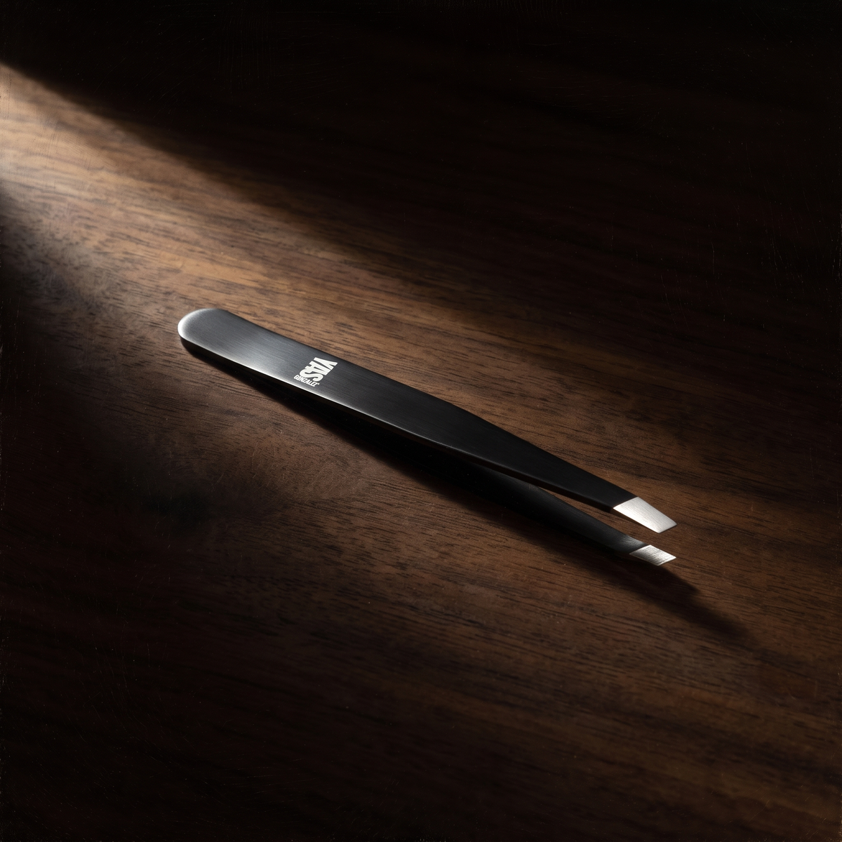 Precision Tweezers de YG Beauty sobre nogal oscuro, luz de claroscuro